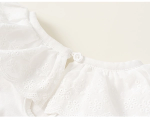 Detail van de witte meisjesjurk met kanten borduursel en bloemvormige knoop op de kraag