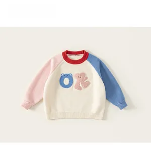 Detail of color-block knit sweater for kids featuring cartoon bear plush patch and ribbed crewneck