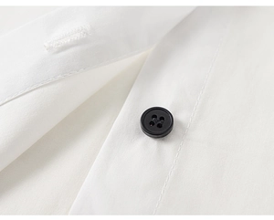 Detail shot of white cotton shirt featuring a black four-hole button and precise stitching