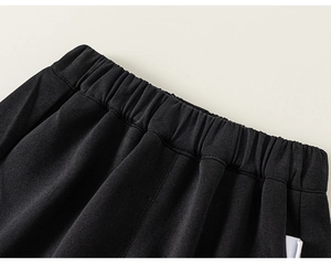 Detail view of the elastic waistband on boys' black knitted trousers with uniform pleats