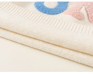 Macro shot of off-white chunky knit texture with colorful towel embroidery and ribbed edge