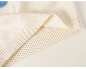 Detail of knit sweater hem featuring ribbed texture and blue contrast patch accent