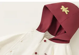 Détail de veste à capuche bicolore pour bébé avec écusson d'ours et boutons rouges