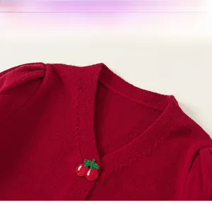 Detailed close-up of a red knit V-neck cardigan with a small cherry patch decoration