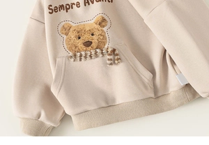Détail du sweat à capuche enfant abricot avec ours en peluche 3D et écharpe à carreaux