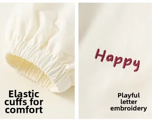 Détail des poignets élastiques et broderie Happy rouge sur manteau blanc crème