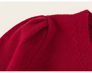Detail view of the red knit cardigan featuring pleated puff shoulder design and texture
