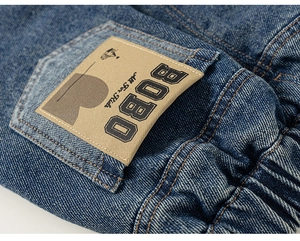 Détail du tissu denim bleu avec étiquette All For Kids et coutures orange sur jean enfant