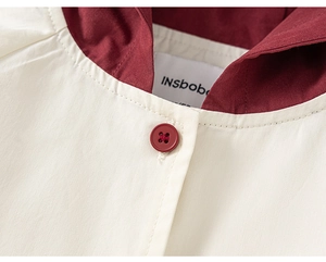 Gros plan du col bordeaux contrasté et du bouton sur la veste coupe-vent enfant