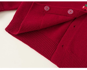 Detail of red girl's knit cardigan featuring ribbed hem and cute cherry embroidery