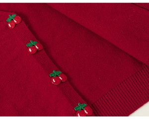 Detailed close-up of knitted red cherry embellishments on a burgundy girls cardigan