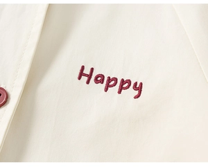Détail de la broderie Happy rouge et du bouton sur la veste beige pour enfants