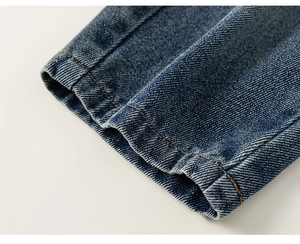 Vue macro d'un ourlet en denim bleu foncé avec surpiqûres orange et effet délavé