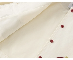 Détail du tissu du coupe-vent beige avec boutons rouges et broderie verte