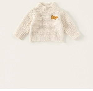 Close-up of cream knit sweater with cute orange cat embroidery and high neck detail