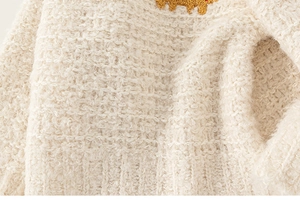 Macro view of cream knit fabric texture with soft granular boucle yarn and yellow embroidery