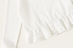 Detail van witte top met lange mouwen en een dubbellaagse rucheszoom van zacht katoenweefsel