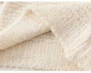 Close-up of cream white fuzzy knit sweater with detailed ribbed hem and textured boucle yarn