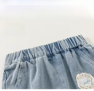 Detail of girls' light blue denim trousers showing elastic waistband and lace floral patch