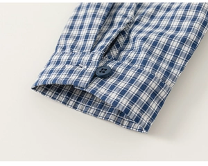 Close-up of blue and white plaid shirt cuff with precise stitching and navy button