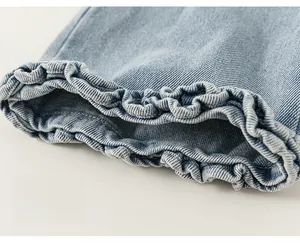 Close-up detail of light blue girls denim jeans featuring ruffled lace hem and twill texture