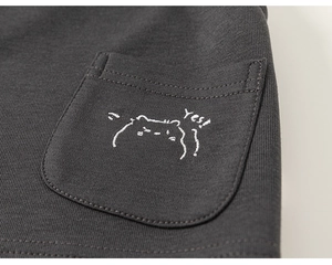 Detail of grey knit fabric showing a round pocket with a cute animal and Yes! embroidery