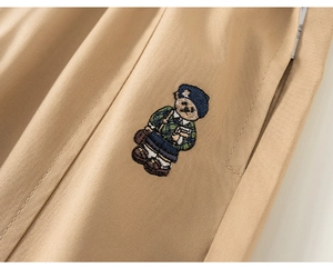 Détail macro de broderie d'ours sur un pantalon enfant en sergé de coton kaki doux