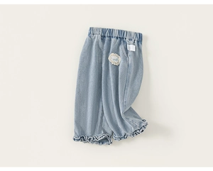 Detail of girls' light blue denim pants featuring ruffled lace trim and embroidered patch