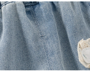 Detail view of girls denim pants with floral embroidery and lace trim on blue fabric