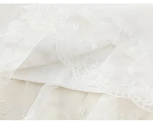 Detail of white mesh fabric with floral embroidery and scalloped lace edges