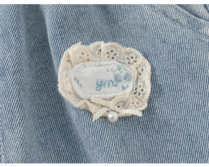 Detailed macro view of lace embroidery and pearl bow on light blue girls' jeans