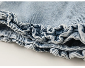 Macro detail of girls' light blue denim trousers showing twill weave and ruffle hem edge