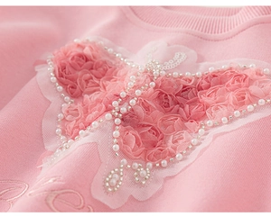 Detailed macro view of 3D pink rose butterfly applique with pearls on girl's sweatshirt
