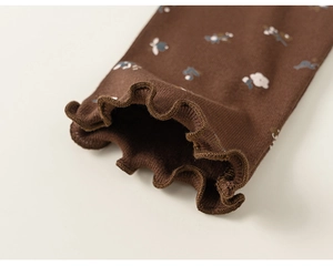 Détail de poignets en maille à volants sur vêtement fleuri marron pour enfant