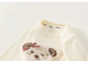 Detailed close-up of cream cotton sweatshirt with plush bear embroidery and lace trim