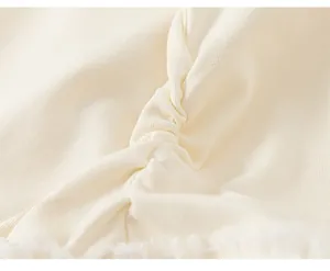 Detailed close-up of the elegant ruched design on the girl's cream long-sleeve T-shirt