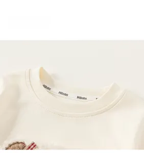 Detail of girls' cream sweatshirt featuring embroidered texture and red plaid bow decoration