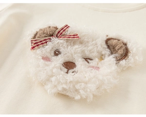Detail of cute white fuzzy teddy bear applique with plaid bow on beige long sleeve t-shirt