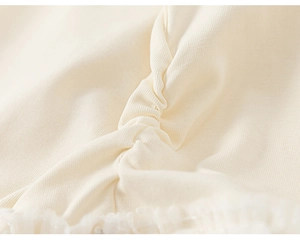 Detailed macro view of cream cotton fabric featuring delicate ruffles and white lace trim