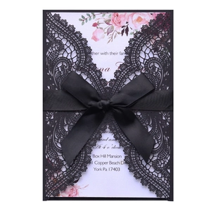 Elegant black laser-cut lace wedding invitation with a satin ribbon bow and floral card