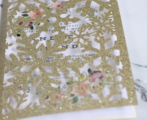 Detail of laser cut gold glitter snowflake invitation with elegant floral inner card