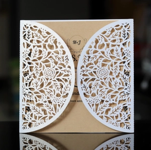 Close-up of laser-cut wedding invitation with lace floral pattern and kraft paper insert