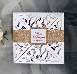 Laser cut wedding invitation with white leaf patterns and a sparkling gold glitter belly band
