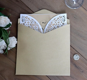 Detail of laser-cut floral wedding invitation with kraft envelope on wooden background