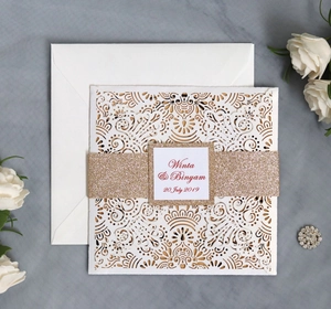 Detail of laser cut wedding invitation with floral pattern and champagne gold glitter band