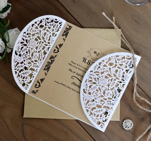 Detail shot of laser-cut floral wedding invitation with kraft RSVP card on wood surface