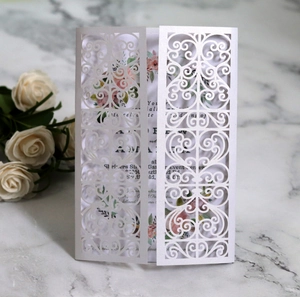 Close-up of white laser-cut floral wedding invitation with intricate lace patterns