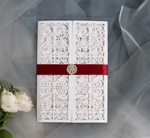 Detail of white laser-cut wedding invitation with red satin ribbon and rhinestone buckle