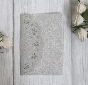 Sparkly silver laser-cut rose floral wedding invitation card on white wood background