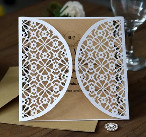 Detail of laser-cut white lace wedding invitation with kraft paper insert and envelope